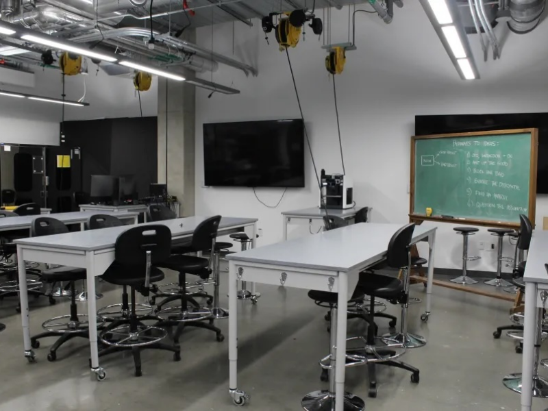 A row of worktables with a chalkboard and televisions mounted on the wall