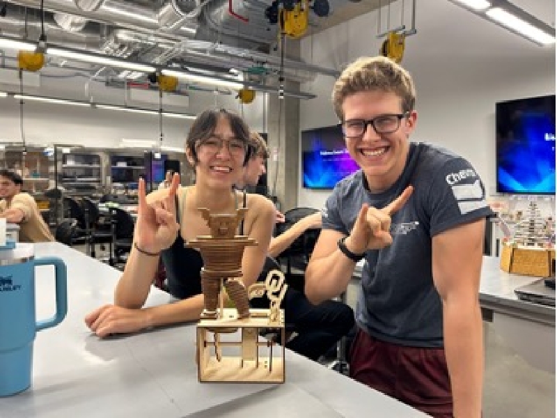 Two UT Students making longhorn symbol with hands and trophy at Lasers Competition